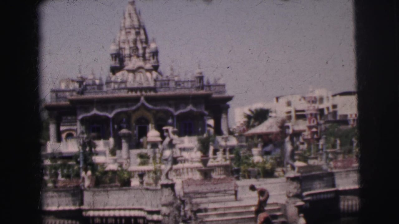 Temple front and spire with people moving along the steps and planted grounds.