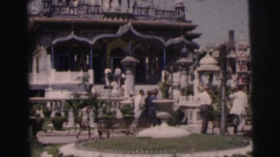 Closer 1962 Calcutta frame showing the temple entrance, decorative columns, lawn, statues or stone ornaments, and visitors nearby.