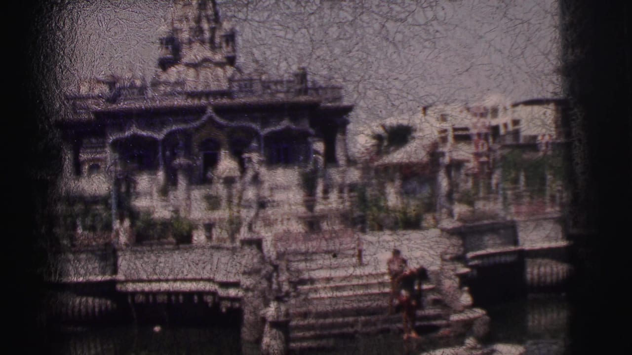Ornate temple beside water with stone steps and small figures nearby.