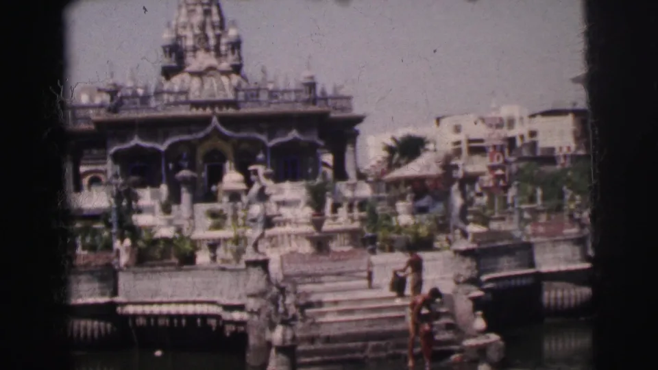 Home-movie frame of a Hindu temple in Calcutta with steps leading toward water and people visible around the foreground.