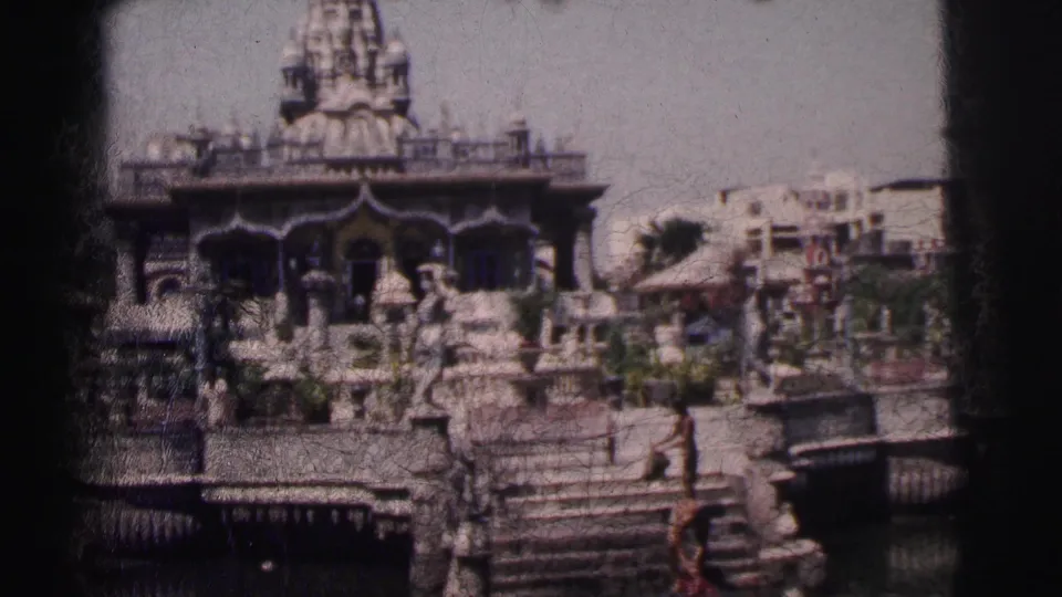 1962 Calcutta 8mm frame showing an ornate temple, water, stone steps, people, and urban buildings in the background.