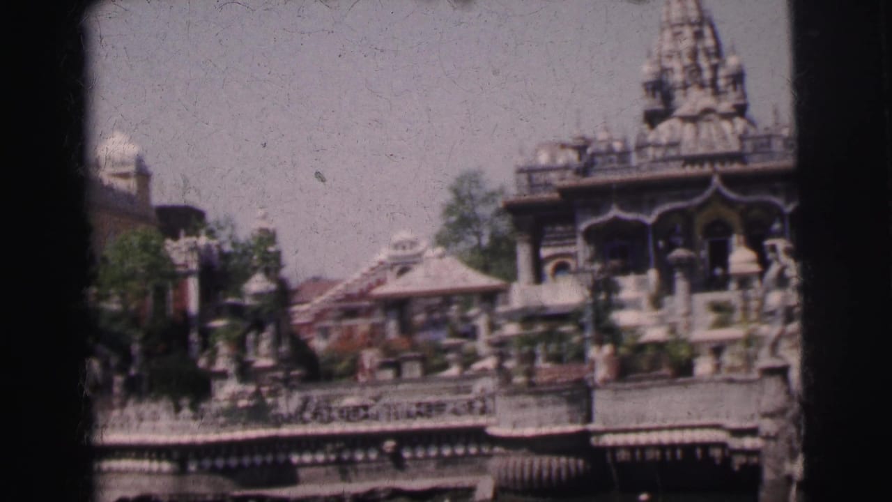 Ornate Indian temple complex with multi-tiered carved spire, decorative stone pavilions, and stone steps seen from across water.