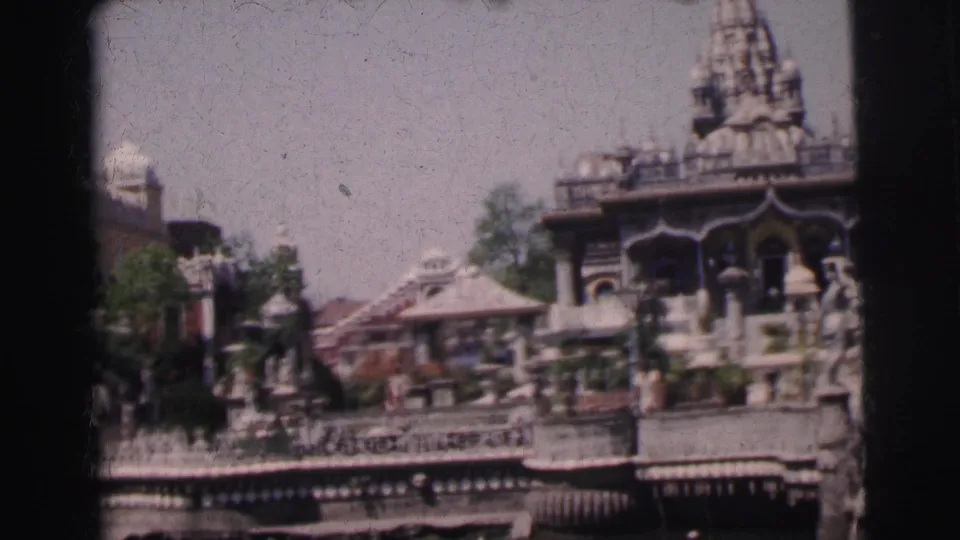 8mm color frame circa 1962 showing an ornate temple complex in Calcutta, India — prominent carved spire, decorative pavilions, and stone steps viewed from across a water body.