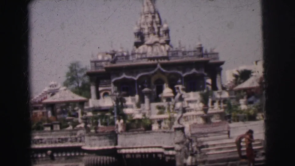 8mm frame circa 1962 showing the Calcutta temple spire prominent at center, carved stone elements, steps to water, and small human figures visible at the base.