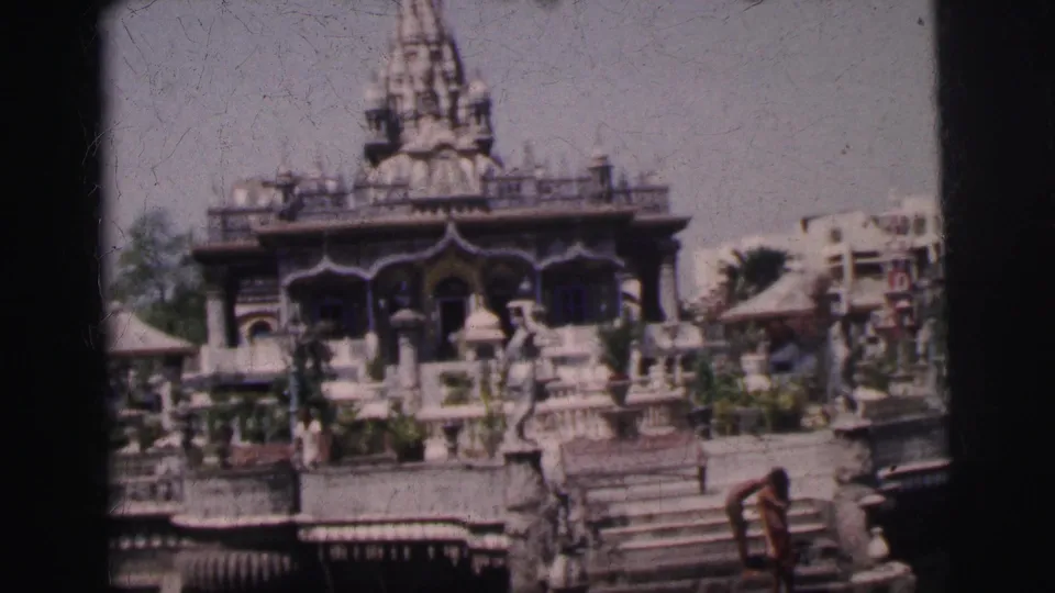 Final 8mm frame circa 1962: Calcutta temple spire and carved stone elements, a person crouching at the water steps in the lower right, and a white building at the right edge.