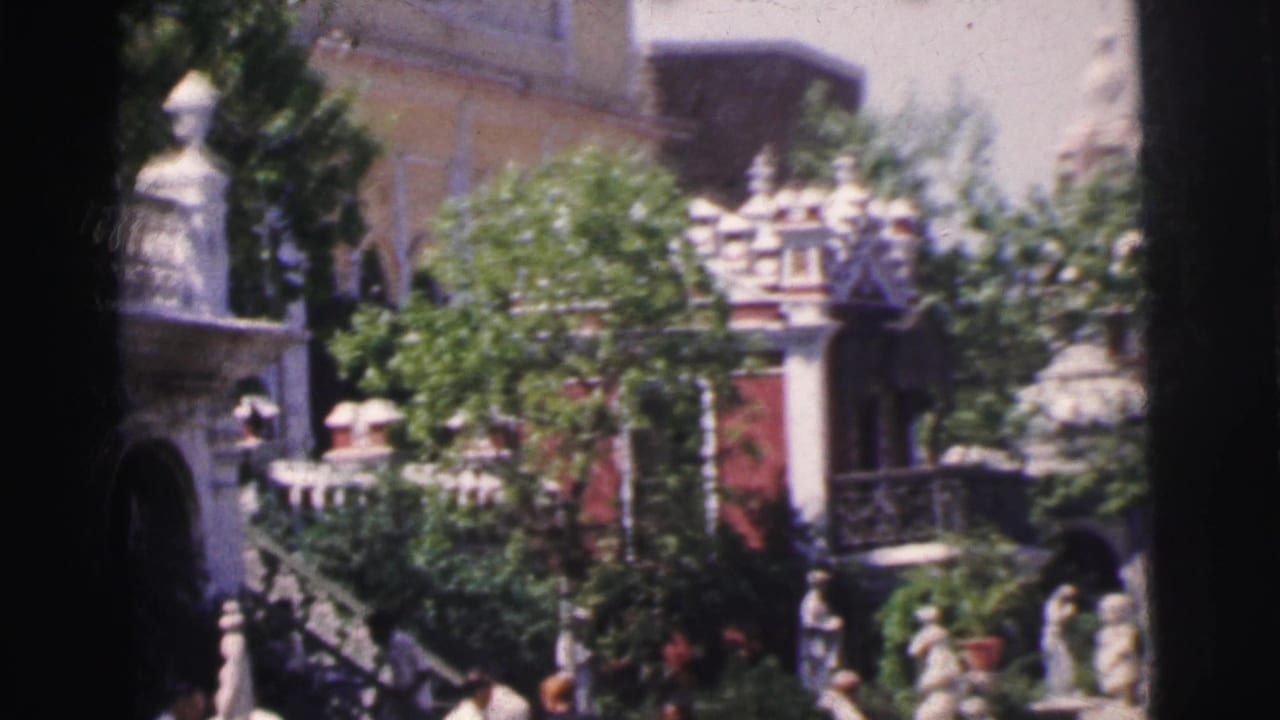Slightly wider view of same ornate building facade with decorative columns, balustrades, and pedestrians, 8mm film.