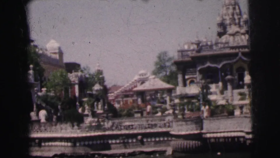 8mm wide shot showing temple spires, domed kiosks, and decorative railings with adult pedestrians on a Calcutta street, circa 1962, mild color fading visible.