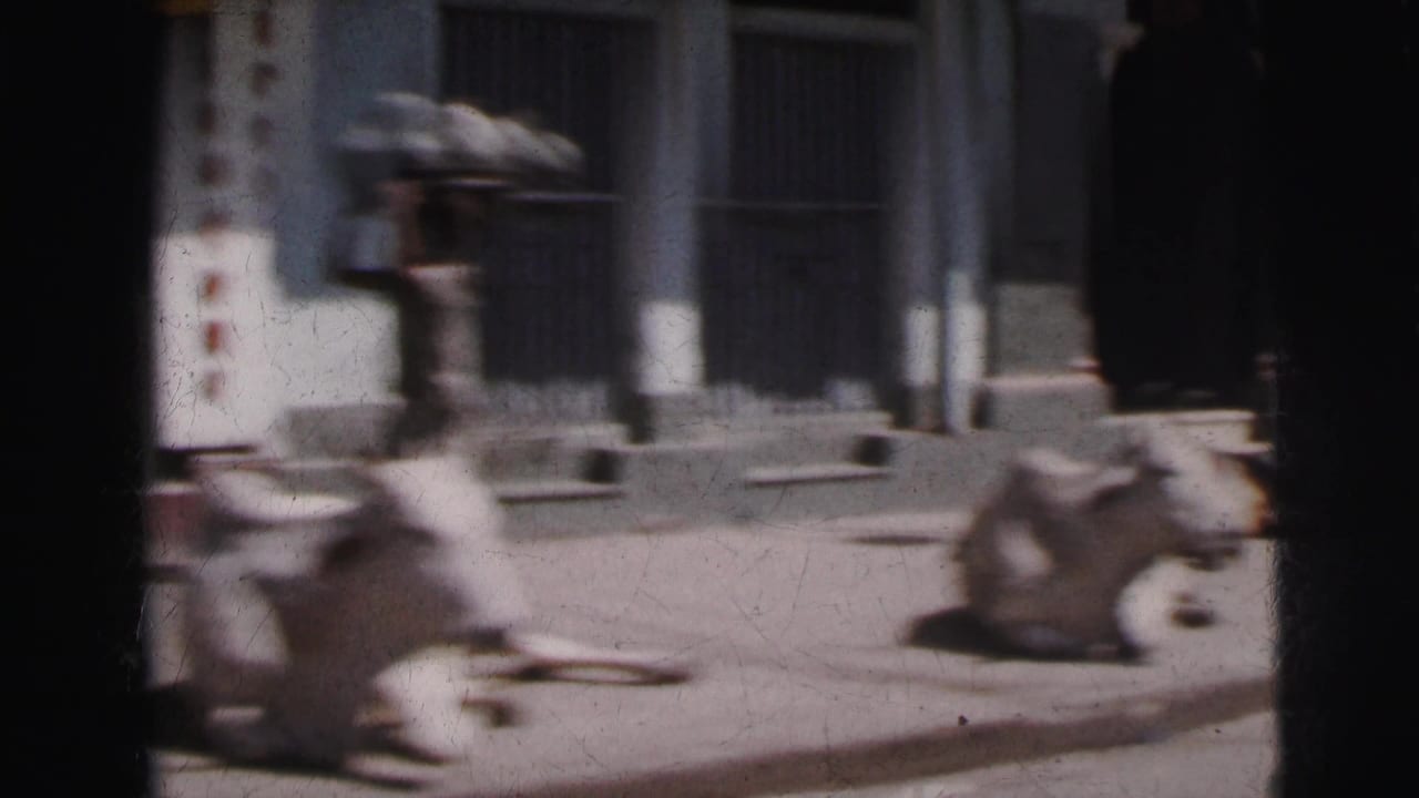 Motion-blurred 8mm frame, c. 1962 Calcutta — cows and pedestrians visible mid-pan past a columned colonial building facade.