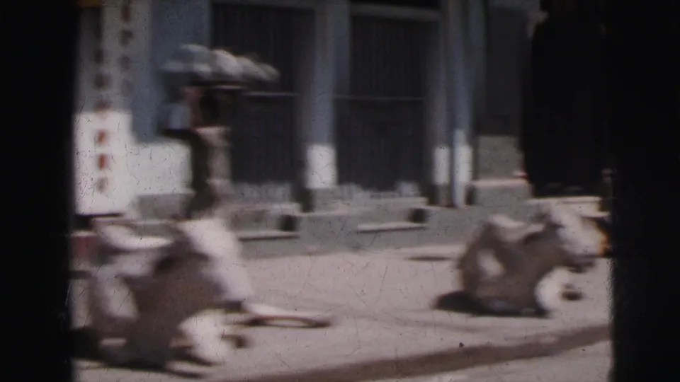 Motion-blurred 8mm frame, c. 1962 Calcutta — cows and pedestrians visible mid-pan past a columned colonial building facade.