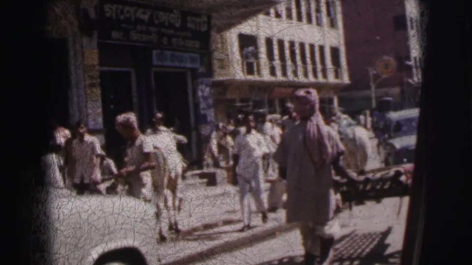 Calcutta, India, c. 1962 — men in traditional white attire and a turban-wearing pedestrian walk a crowded pavement; Bengali-script shop sign above, cows in foreground.