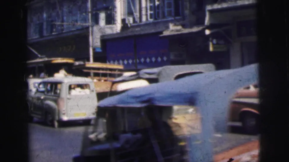 1962 Calcutta street view with a yellow and red trolley in traffic, a white van, and blurred foreground vehicle movement.