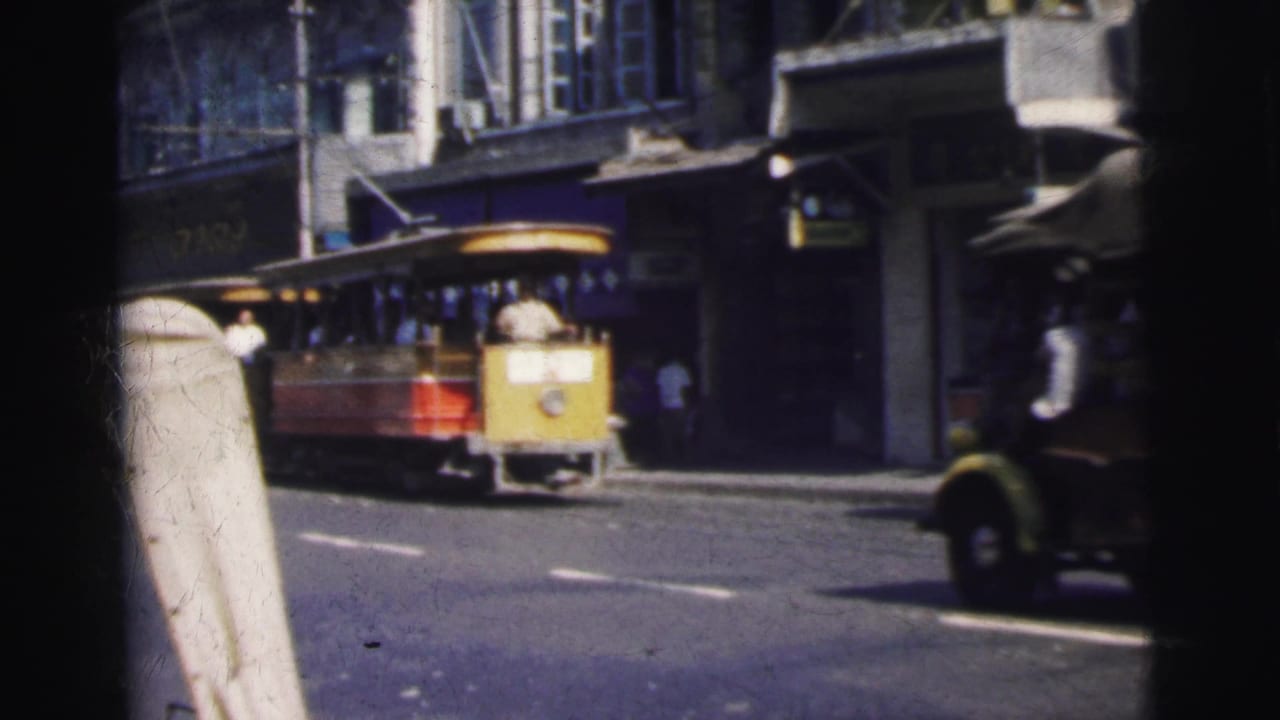 Yellow and red trolley passes storefronts as vehicles move along the road.