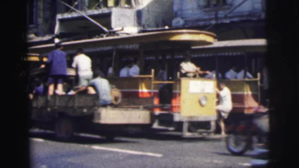 In 1962 Calcutta, people are visible around the rear of a yellow and red trolley as mixed traffic passes nearby.