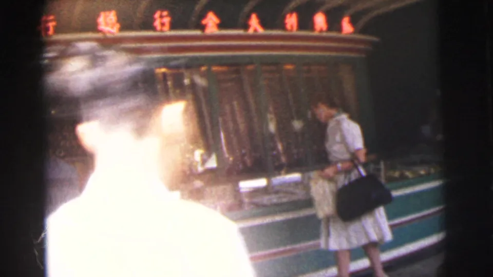 1962 Calcutta footage frame showing a woman from behind at a dim shop counter with red signage overhead.
