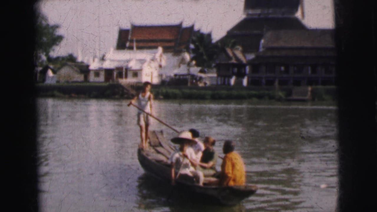 1962 Calcutta 8mm frame showing a wooden river boat with a standing paddler, seated passengers, and waterfront buildings behind them.