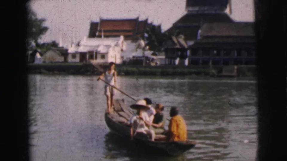 1962 Calcutta 8mm frame showing a wooden river boat with a standing paddler, seated passengers, and waterfront buildings behind them.