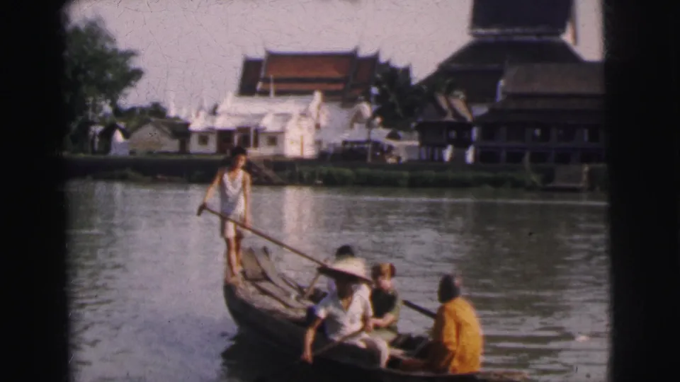 1962 Calcutta 8mm still with a standing paddler, seated passengers, and riverside architecture in the background.
