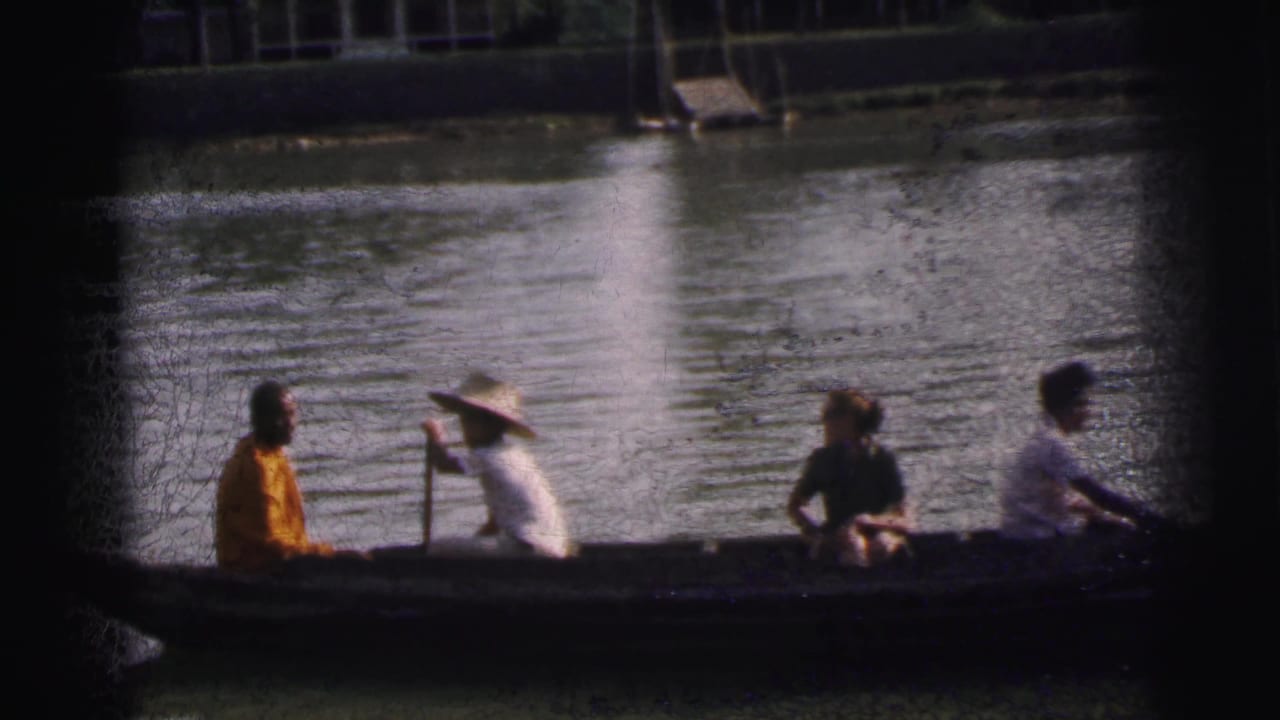 Home-movie view in Calcutta, India, with a broad-hatted guide paddling a canoe carrying passengers across rippled water.