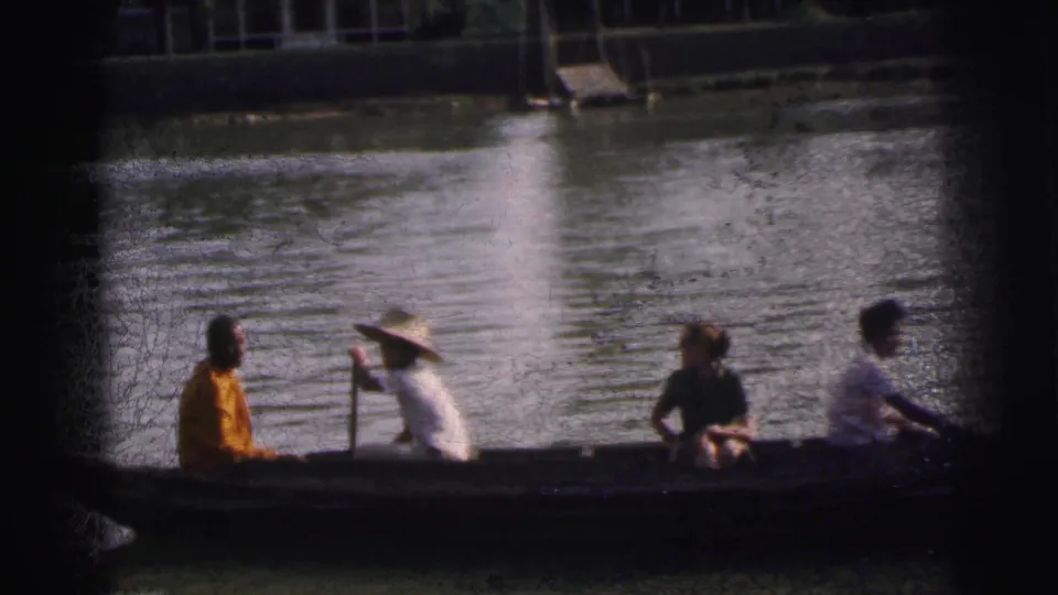 Home-movie view in Calcutta, India, with a broad-hatted guide paddling a canoe carrying passengers across rippled water.