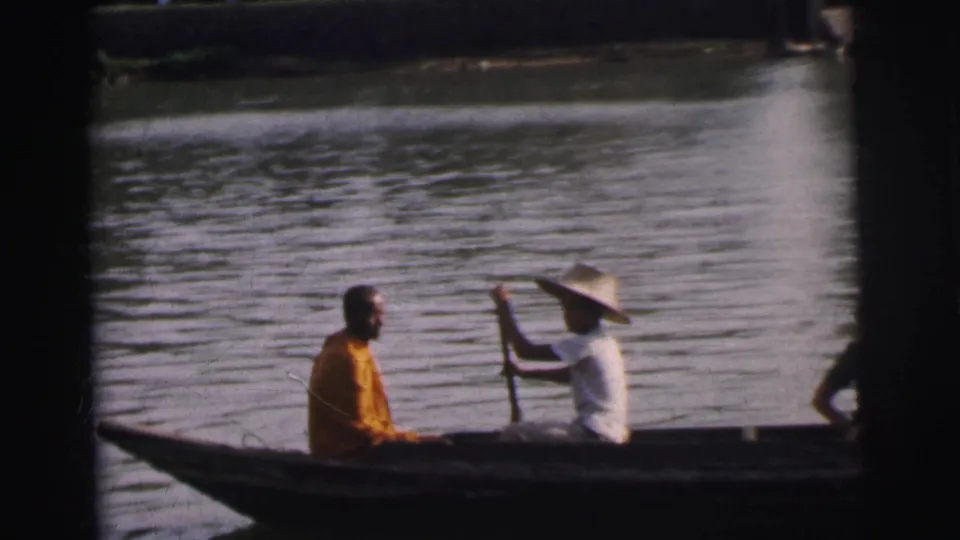 1962 Calcutta river footage showing a long canoe with an orange-robed passenger near the bow and a guide paddling opposite him.