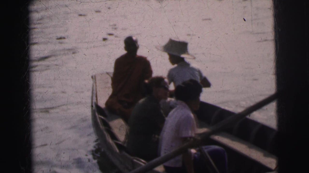 1962 Calcutta home-movie frame showing seated passengers in a wooden boat, including a saffron-robed monk near the bow.
