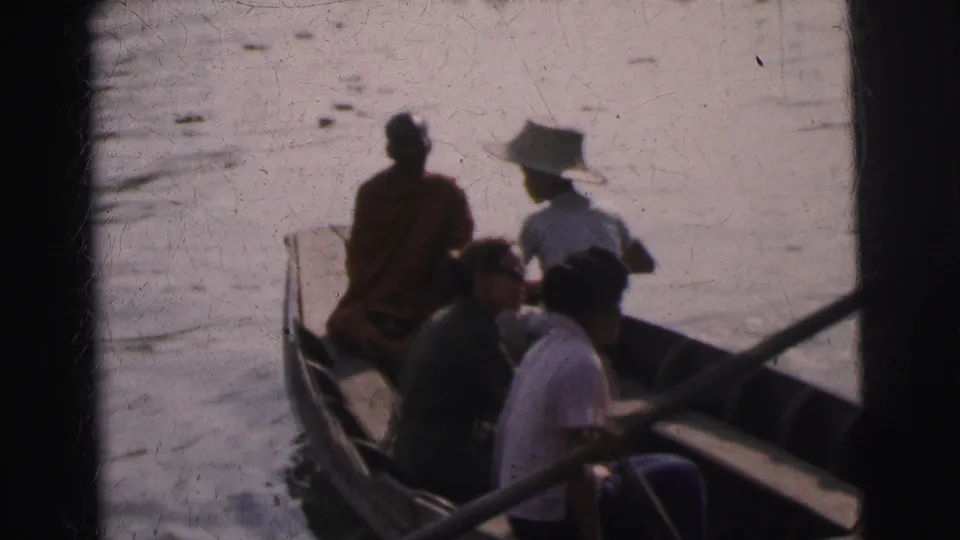 1962 Calcutta home-movie frame showing seated passengers in a wooden boat, including a saffron-robed monk near the bow.