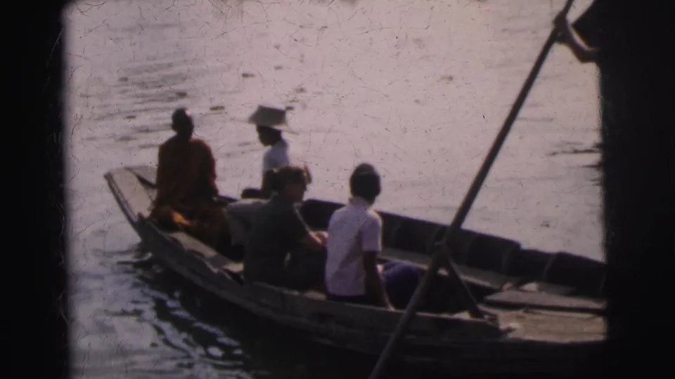 1962 Calcutta 8mm frame of seated passengers in a wooden boat, with a robed figure and hat-wearing passenger visible.