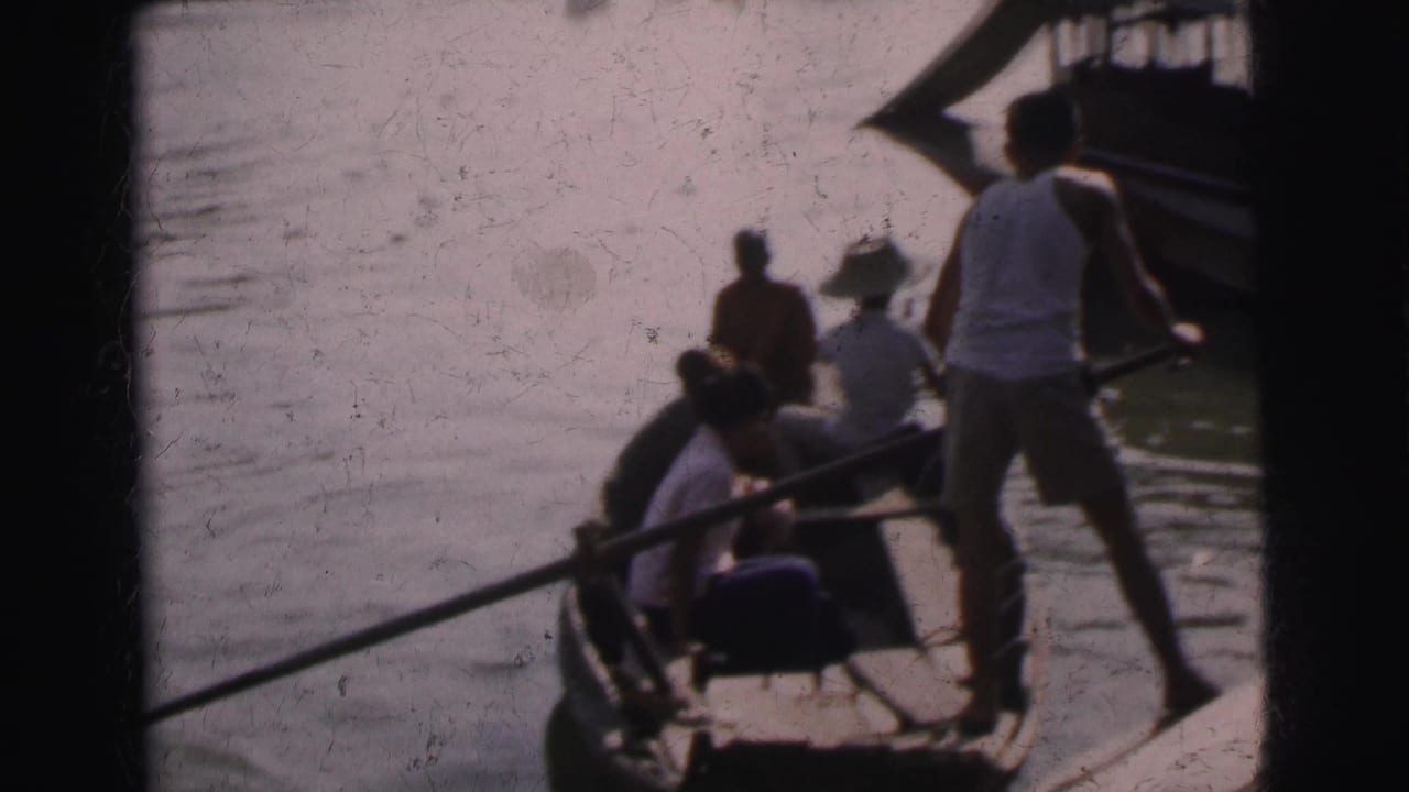 1962 Calcutta home-movie frame showing travelers in a small wooden river boat with a standing boatman near the bow.