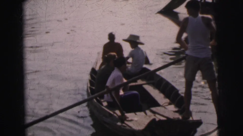 1962 Calcutta home-movie view of travelers seated in a wooden river boat as a standing man handles a pole.