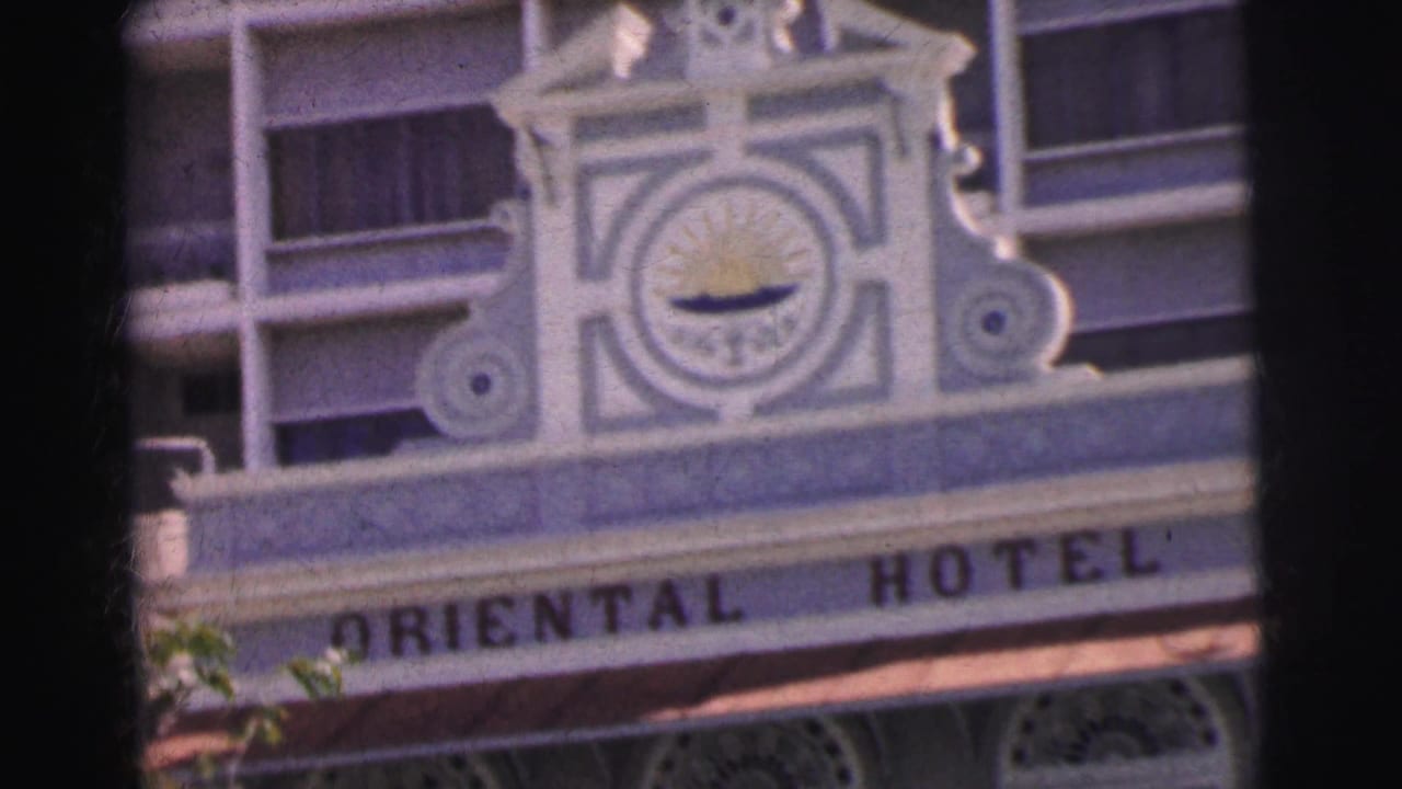 1962 Calcutta 8mm frame showing the Oriental Hotel name beneath an ornate facade with a sun emblem and balconies behind it.
