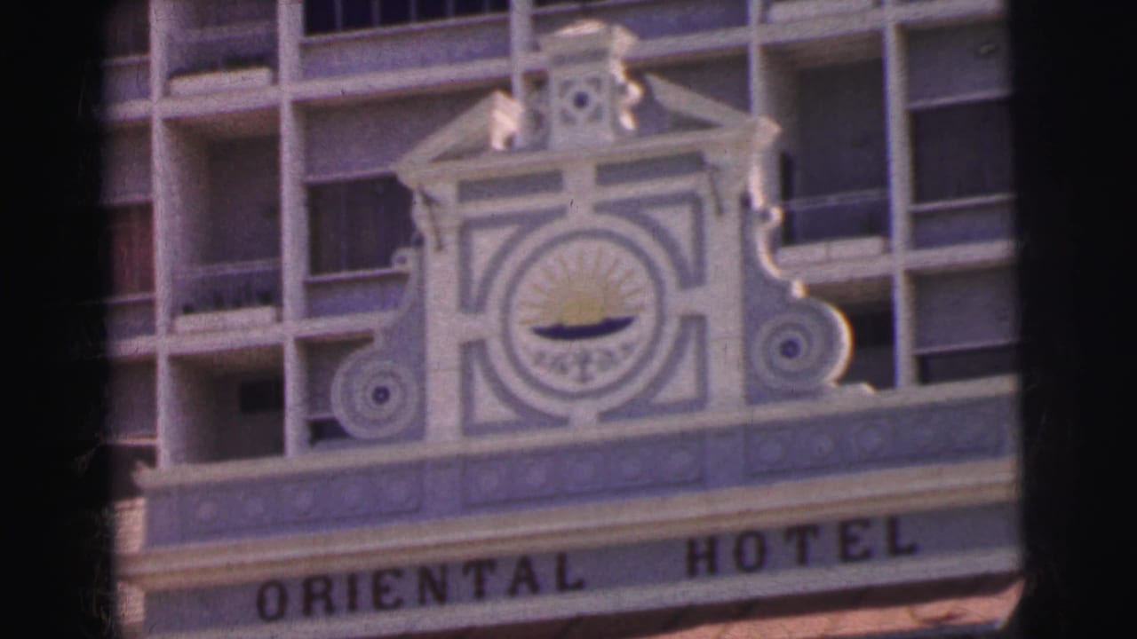 1962 Calcutta 8mm frame of the Oriental Hotel sign, decorative crest, and gridded hotel windows seen in soft focus.