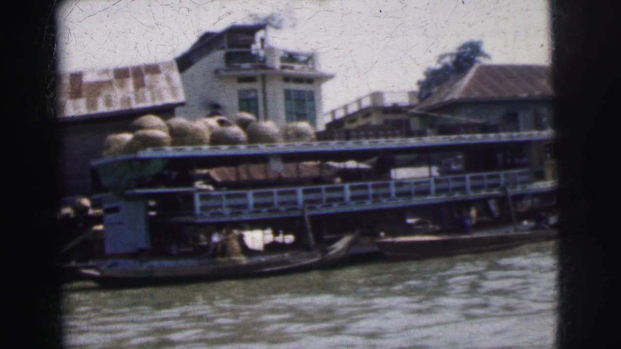 1962 Calcutta home-movie frame showing a loaded cargo boat near riverside buildings, filmed from across the water.
