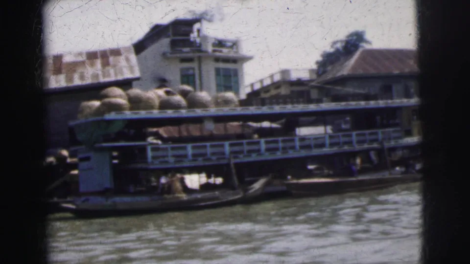1962 Calcutta home-movie frame showing a loaded cargo boat near riverside buildings, filmed from across the water.