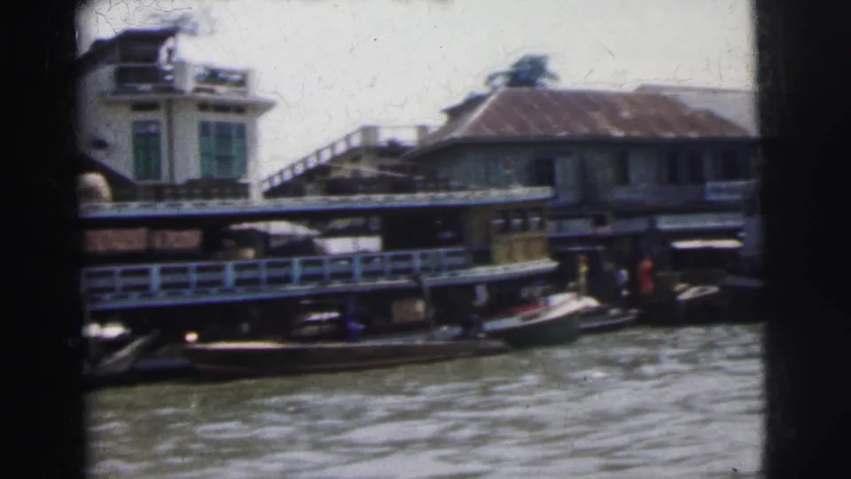 1962 Calcutta river view with a cargo boat, waterfront structures, railings, and small craft along the bank.