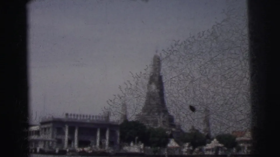 1962 Calcutta home-movie view of a tall temple spire beyond trees, with a riverside building and water in the foreground.