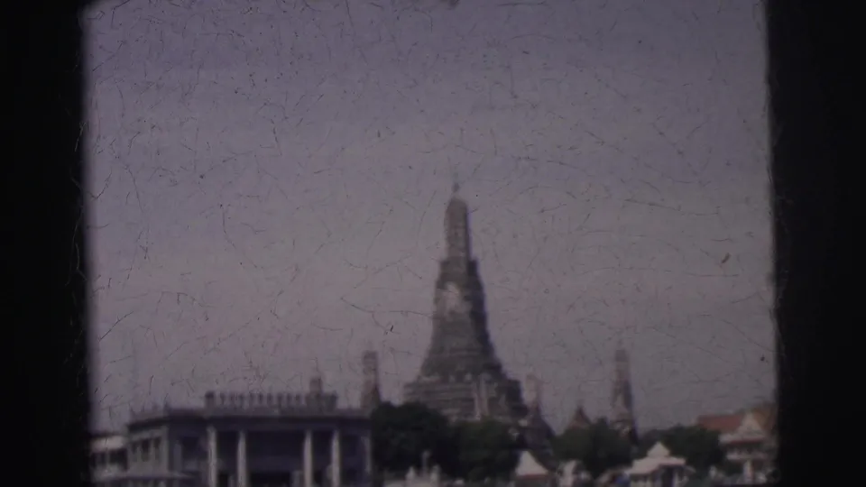 1962 Calcutta river view with a distant temple spire, trees, rooftops, and waterfront structures under faded 8mm color.
