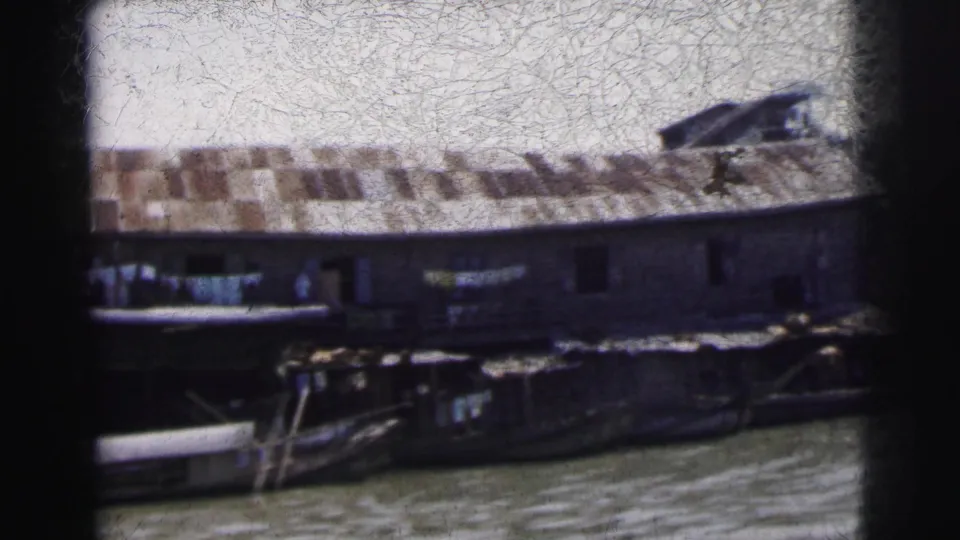 Soft 8mm view of a Calcutta waterside building, moored boats, dock details, and market goods along the river.