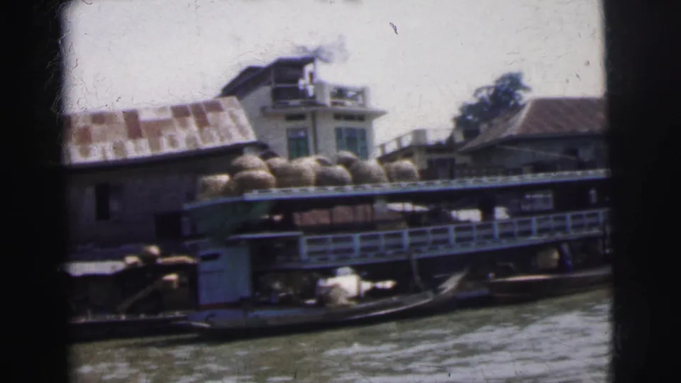 1962 Calcutta river scene with a larger boat, piled basket cargo, railings, waterfront houses, and people near the market area.