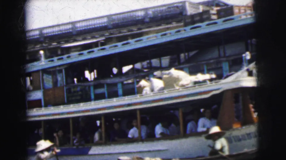 A large river passenger vessel in Calcutta, India, with seated passengers and small boats crossing near its side.