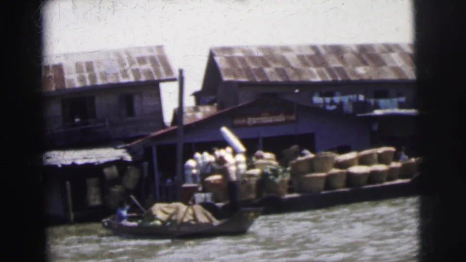 Calcutta waterfront view with sheds, stacked goods, and a small wooden boat moving along the riverbank.