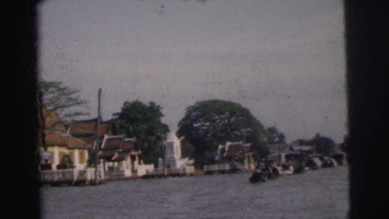 Waterway with ornate riverside buildings, trees, and small boats in the distance.
