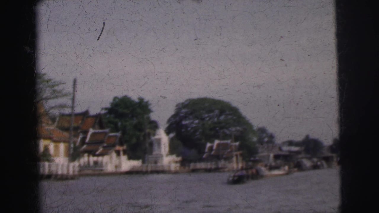 1962 Calcutta 8mm frame with a small boat crossing a broad waterway near roofed buildings and trees.