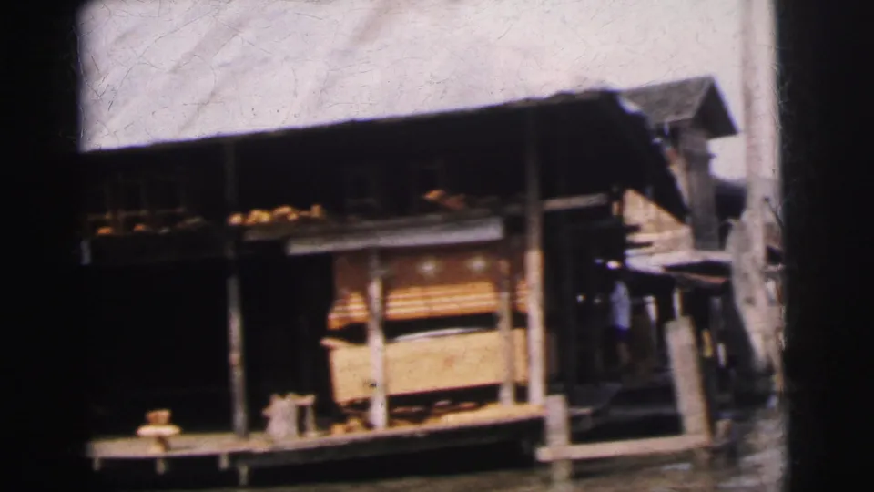 1962 Calcutta home-movie frame showing a wooden boathouse-like structure on the river, with a raised platform and roof.