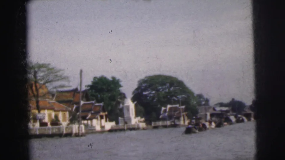 Wide 1962 Calcutta riverfront view with trees, temple-like buildings, and small boats moving across the water.