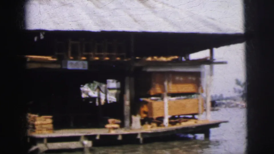 A Calcutta waterfront shop on wooden supports, with stacked goods and a dock platform visible in 1962 footage.