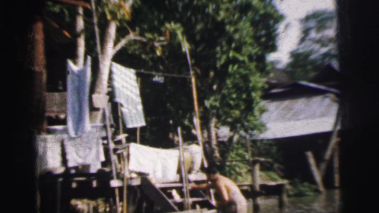 Raised house, laundry, trees, and an adult standing near floodwater.