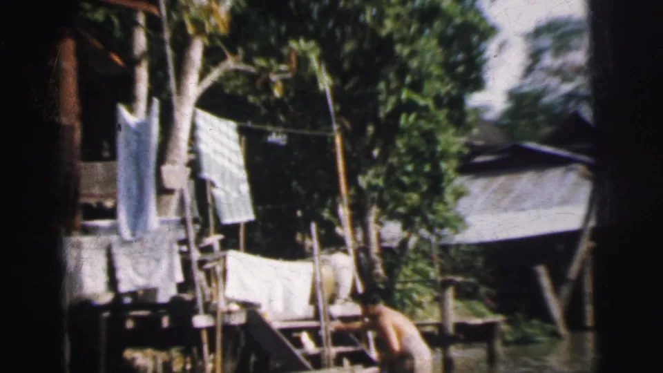 1962 Calcutta frame with laundry hanging beside a raised waterside dwelling and an adult near the flooded edge.