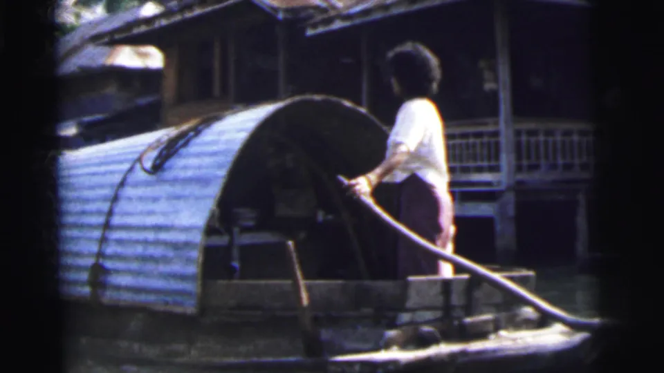 Adult steers a covered wooden boat along a Calcutta waterway, with raised houses and balconies in the background.
