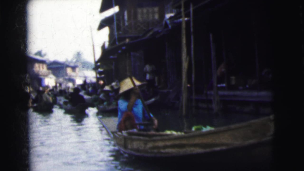 1962 Calcutta home-movie frame showing boats on a crowded canal beside wooden waterside structures and seated people.