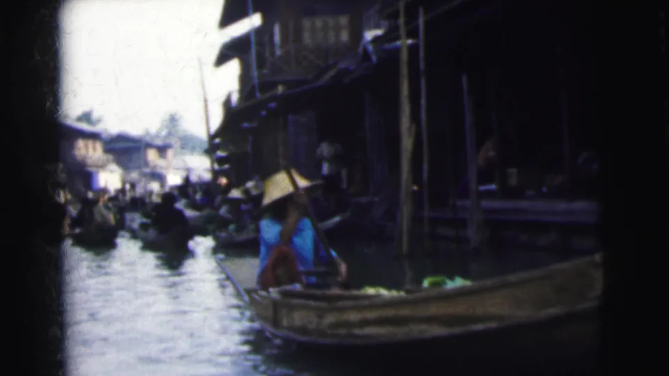 1962 Calcutta home-movie frame showing boats on a crowded canal beside wooden waterside structures and seated people.